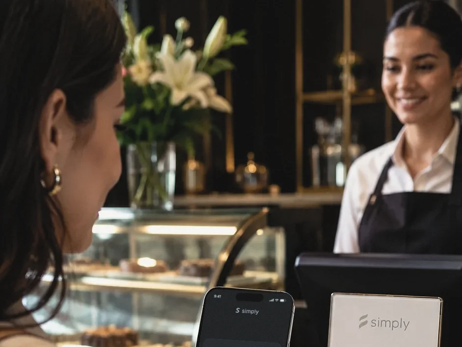En el mostrador de un café, una cajera sonríe a una clienta que acaba de pagar con su teléfono.
