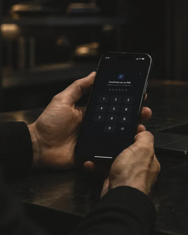 Dos manos sostienen un teléfono con la app de Simply abierta: pide el PIN para confirmar una transferencia.